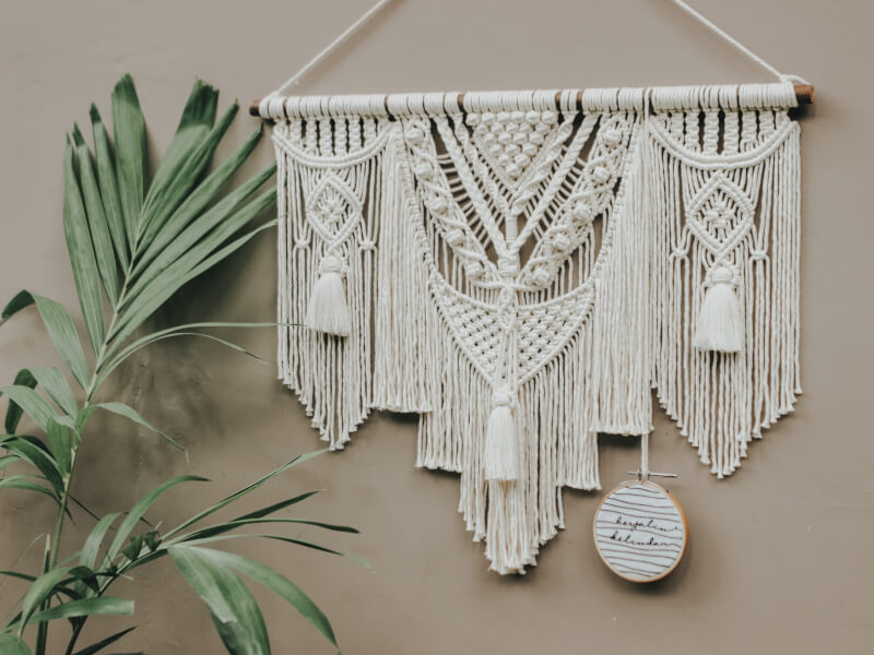 Macrame wall hanging in an intricate white cotton design with wooden hanger